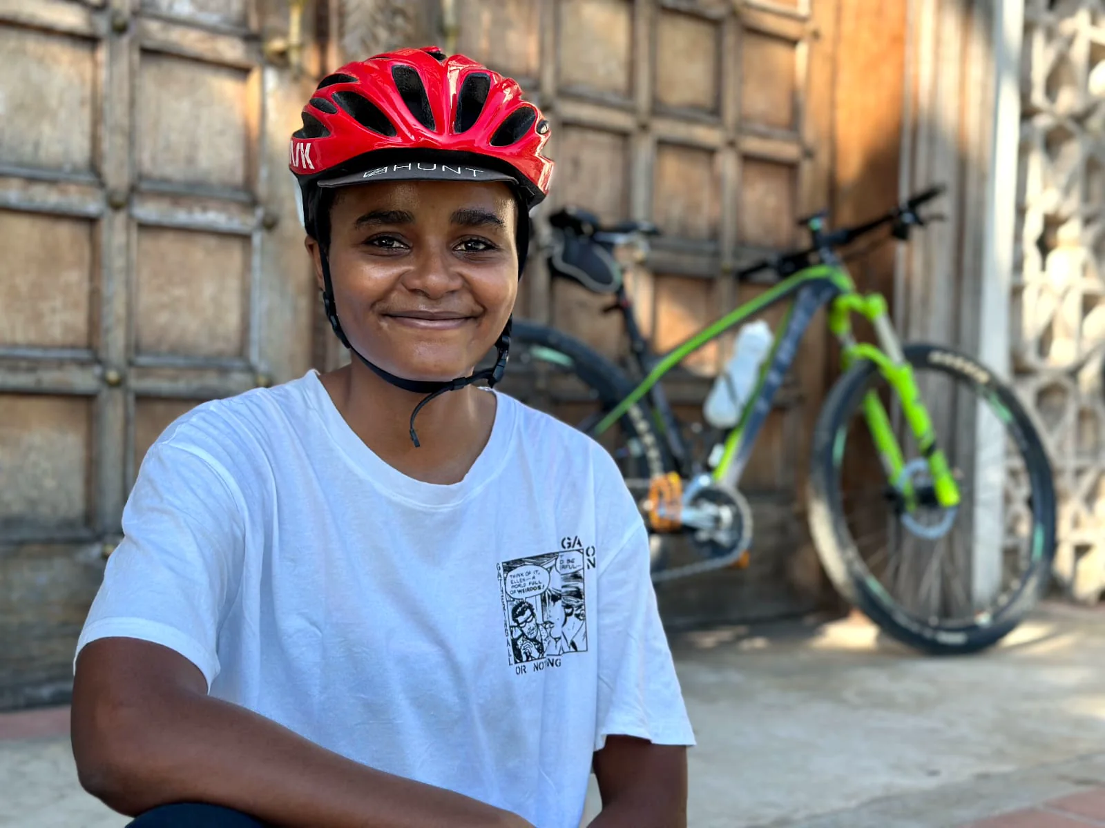 Iman Kagumba sitting beside a mountain bike while wearing a cycling helmet
