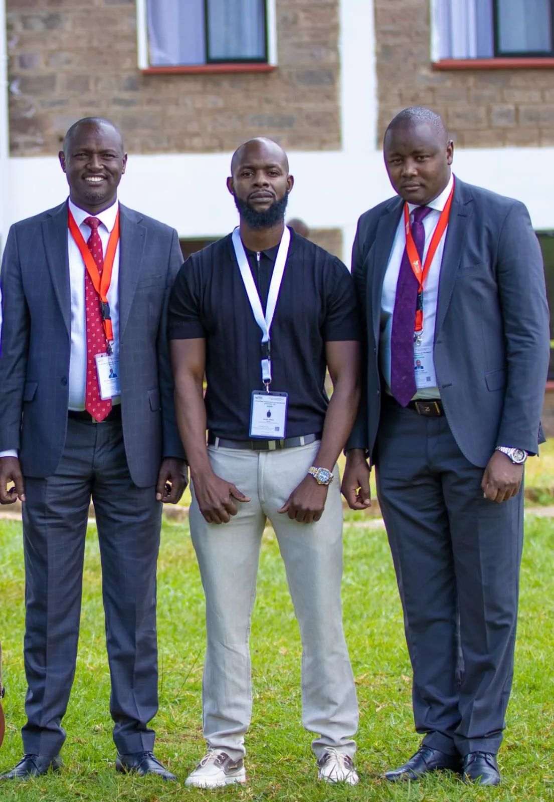 Three men wearing conference delegate lanyards outside a stone building