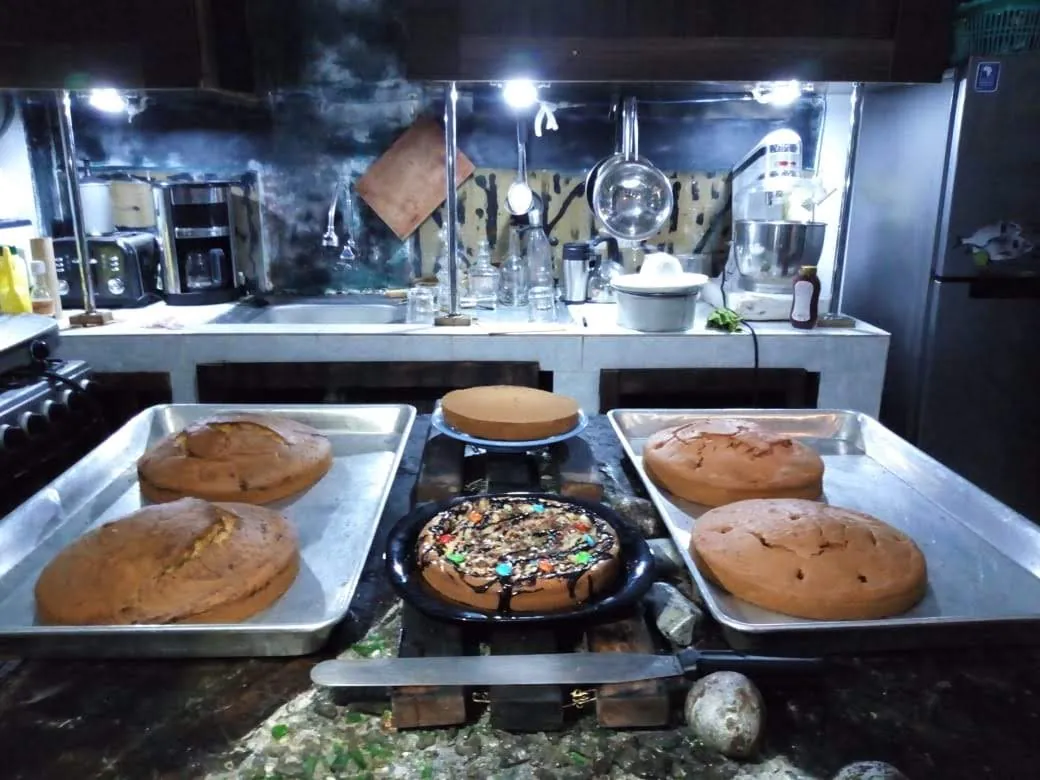 Several large baked cakes cooling on steel trays in a production kitchen