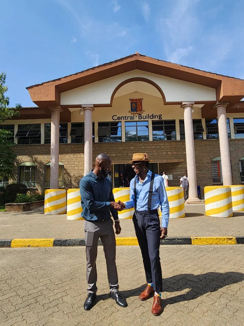 Two men shaking hands on a paved forecourt outside a building signposted Central Building