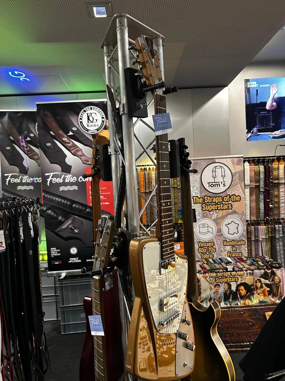 Trade stands at a guitar industry fair, with instruments on a rack and manufacturers' banners behind