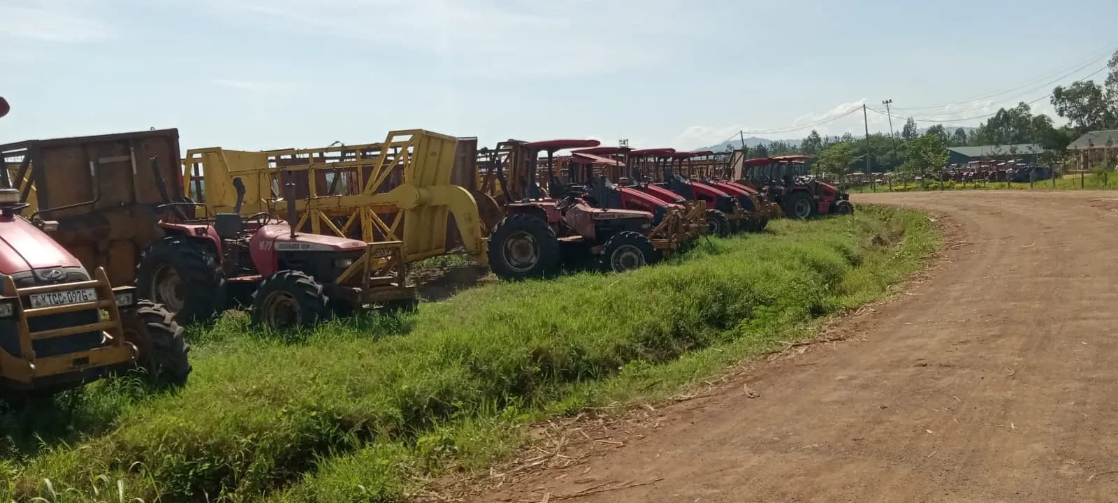 A long line of tractors and farm implements parked along a dirt road