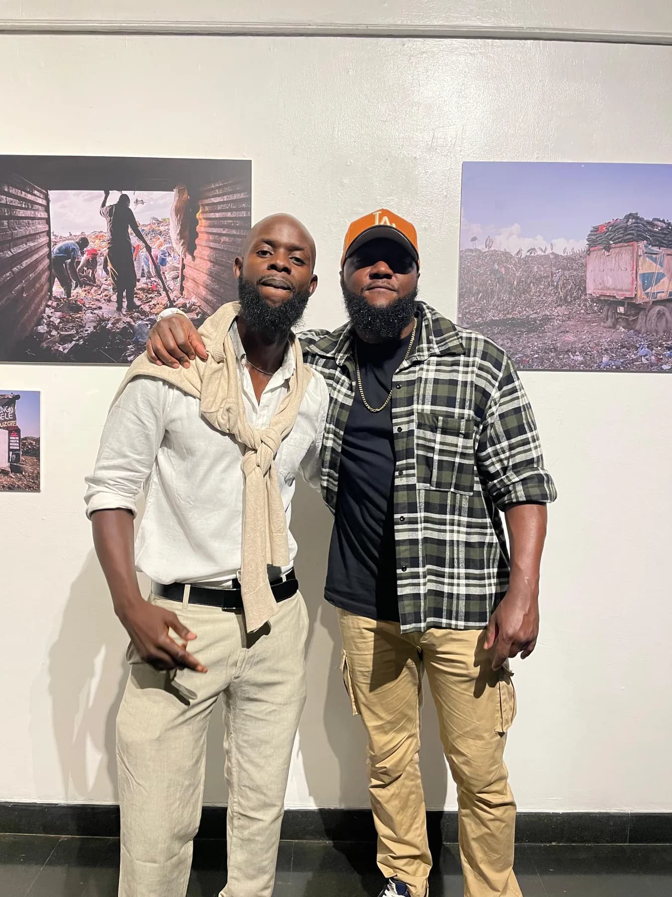 Two men standing in a gallery in front of large mounted documentary photographs of a waste site