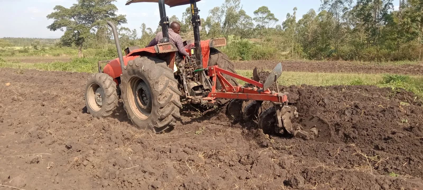 A red tractor pulling a disc plough through dark soil