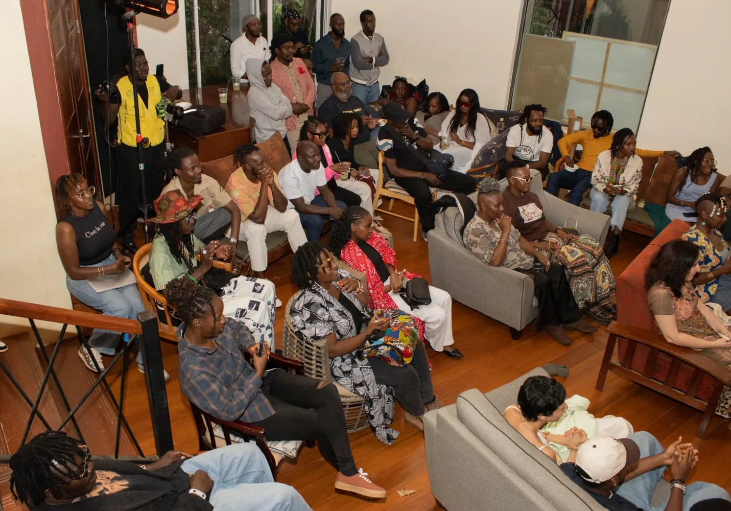 A full room of people seated on chairs and sofas facing a performance