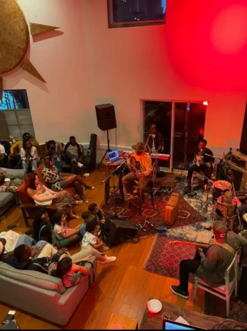 A wide view of a double-height room lit red, with a band playing to an audience seated on the floor and on sofas